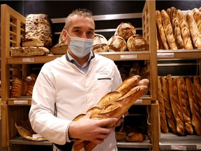 French baker Mickael Reydellet, wearing a protective face mask, poses with freshly-baked baguettes at "La Parisienne" bakery in Paris, France, February 17, 2021. Picture taken on February 17, 2021.