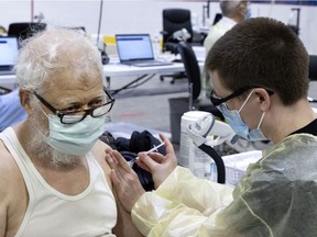 A healthcare worker administers the COVID-19 vaccination to Akm Huba, 75, at a clinic inside the Bill Durnan Arena in Montreal on Wednesday, March 10, 2021.