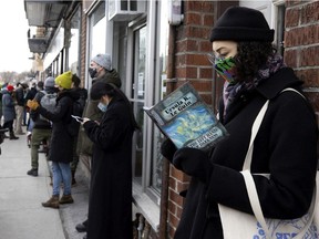 Trynne Delaney reads while in a long line on St-Viateur St. during a "read-in" protest to symbolize opposition to predatory landlords, outside S.W. Welch Bookstore, in Montreal, on Saturday, March 13, 2021.