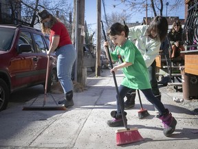 Siblings Nova, front, and Milo Newman, right, help clean up their front sidewalk on Henri Julien av., with neighbour Katie Jung, red, on Wednesday March 17, 2021.