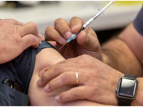 Vaccine administrator Pascal Aoude gives Marc-Andre Chene his first of two Pfizer vaccine shots at the Dollard Civic Centre in Dollard-des-Ormeaux on Thursday March 25, 2021.