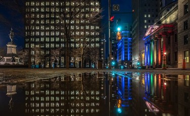 The rainbow colours on the Bank of Montreal are reflected in a puddle at Place d'Armes in Montreal on April 21, 2020.
