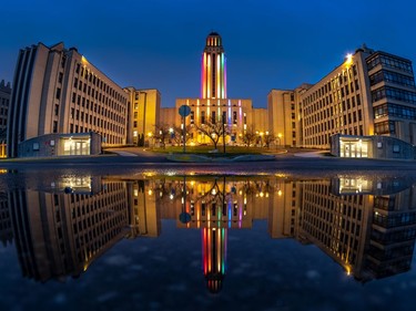The University of Montreal, reflected in a puddle, has lit their centre tower in rainbow lights on April 29, 2020.