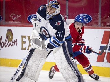 Canadiens' Brendan Gallagher (11) skates past Winnipeg Jets goaltender Connor Hellebuyck behind the net during NHL action in Montreal on Saturday, March 6, 2021.