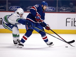 Vancouver Canucks defenceman Quinn Hughes (43) grimaces as he tries to tap the puck away from Canadiens' Tomas Tatar (90) during NHL action in Montreal on Saturday, March 20, 2021.