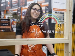 Maroua of the St. Henri Home Depot works behind a plexiglass barrier decorated with a 'Ca va bien aller' rainbow on March 27, 2020.
