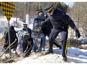 RCMP officers help a group of asylum seekers to jump a ditch as they crossed from the U.S. into Canada illegally at the border at Roxham Road in Hemmingford,  south of Montreal, on  Feb. 20, 2017.