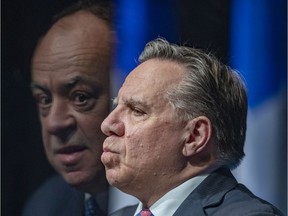 Quebec Premier François Legault listens as Health Minister Christian Dubé, reflected in a plexiglass divider, answers a question during a press conference in Montreal Tuesday April 6, 2021.