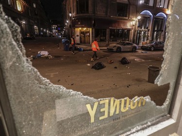 Workers look over damage on rue Notre-Dame West outside of Rooney Shop in Old Montreal Sunday, April 11, 2021. A crowd of at least several hundred people gathered at the Old Port, chanting and shooting off fireworks and causing damage to protest the return to an 8 p.m. curfew in Montreal.
