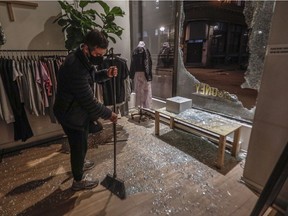 MONTREAL, QUE.: APRIL 11, 2021 --Alex Danino, owner of a clothes store called Rooney Shop in Old Montreal sweeps up glass from a broken window made when a crowd of at least several hundred people gathered at the Old Port, chanting and shooting off fireworks and causing damage to protest the return to an 8 p.m. curfew in Montreal. (John Kenney / MONTREAL GAZETTE) ORG XMIT: 66009