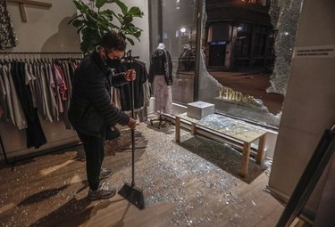 Alex Danino, owner Rooney in Old Montreal, sweeps up glass from a broken window made when a crowd of at least several hundred people gathered at the Old Port, chanting and shooting off fireworks and causing damage to protest the return to an 8 p.m. curfew in Montreal.