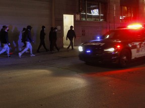A Montreal police cruiser drives by a group of young men in downtown Montreal Monday, April 12, 2021. Protesters against COVID-19 restrictions set by the Quebec government were out after the 8:00 p.m. curfew.
