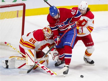 Goalie Jacob Markstrom fights through screen by Montreal Canadiens' Joel Armia, checked by Flames' Rasmus Andersson, for the loose puck during first period at the Bell Centre in Montreal on Wednesday April 14, 2021.