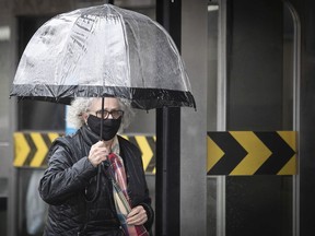 A woman leaves the Lionel-Groulx metro by covering up with mask and umbrella.