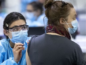 A health-care worker checks on a woman as she administers a COVID-19 vaccination at the Bill Durnan Arena in Montreal on Wednesday, April 21, 2021.