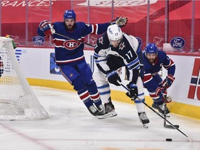 Adam Lowry (17) of the Winnipeg Jets skates the puck in between Canadiens' Joel Edmundson (44) and Shea Weber ()6 during the first period at the Bell Centre on Saturday, April 10, 202, in Montreal.