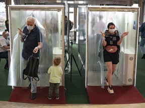 People wearing face masks and gloves to protect against coronavirus come through passages equipped with disinfectant sprays at a shopping mall entrance in Moscow, Russia, Monday, Aug. 3, 2020. While the masks are helpful, spraying people with disinfectant probably is not.