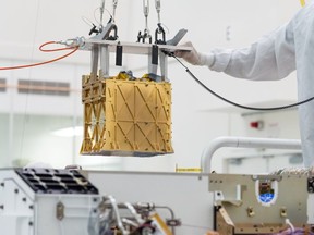 Technicians at NASA's Jet Propulsion Laboratory lower the Mars Oxygen In-Situ Resource Utilization Experiment (MOXIE) instrument into the belly of the Perseverance rover in an undated photograph in Pasadena, California, U.S.