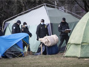 Montreal police officers walk along tents set up at a makeshift campground on Notre-Dame St. in December. They may be asked once again to forcibly remove homeless people who have set up camp on government land on Hochelaga St. further east.