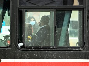 People wearing protective masks board a city transit bus during the COVID-19 pandemic in Toronto, Feb. 19, 2021.