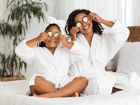 Playful black mother and daughter in bathrobes applying cucumber pieces to eyes