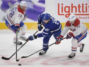 Maple Leafs forward John Tavares (91) tries to skate the puck against Canadiens defenceman Jon Merrill (28) and forward Ryan Suzuki (14) in the first period at Scotiabank Arena in Toronto on Saturday, May 8, 2021.