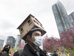 A man wears a cardboard house on his head during a demonstration calling for more affordable and social housing in Montreal, Saturday, May 8, 2021.