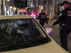 A police officer looks at damage to a car on rue Notre-Dame St. W. in Old Montreal on Sunday, April 11, 2021. A crowd of at least several hundred people gathered at the Old Port, chanting and shooting off fireworks to protest against the return to an 8 p.m. curfew in Montreal.