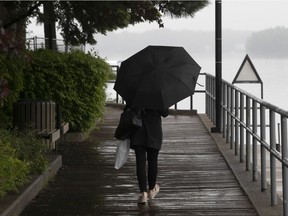 A woman walks, with umbrella in hand, along the pathway on the Ste-Anne boardwalk on Thursday June 3, 2021.