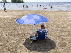 A man reads in his little spot of shade as people try to beat the heat at Cap-Saint-Jacques beach in Montreal, on Monday, June 28, 2021.