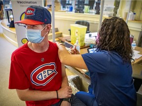 Montreal Canadiens fan Michael Scott looks away as nurse Daniele Richard vaccinates him during vaccination clinic at the Douglas Institute in Verdun on June 30, 2021.
