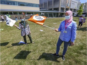 Orderlies Amal A, left, and Maroi Dobli wave flags during a demonstration by health-care workers outside Maisonneuve-Rosemont Hospital in Montreal on Wednesday May 27, 2020.