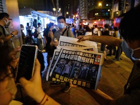 People take photos of a copy of the latest Apple Daily newspaper in Hong Kong early on June 18, 2021, after Hong Kong police arrested the chief editor and four executives of the pro-democracy newspaper the day before, raiding its newsroom for a second time in the latest blow to the outspoken tabloid.