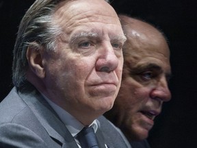 Quebec Premier Francois Legault listens to Quebec Minister of Economy and Innovation Pierre Fitzgibbon who is reflected in a plexiglass separator during an announcement in Montreal on Wednesday, December 16, 2020.