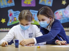 Grade 4 students Mathilde Benjamin, left, and Béatrice O'Doherty wear masks while working together at John Caboto Academy in Monreal on March 8, 2021. The provincial government announced Wednesday that masks will no longer be mandatory in classrooms this fall.