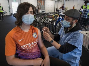 Raphaël Beaudoin gets a COVID-19 vaccine shot from Geoffrey Truchetti at a walk-in (or bicycle ride-in) vaccination centre at the Circuit Gilles Villeneuve in May. Only 16 per cent of Quebecers among those aged 18 to 29 has received two vaccine doses.