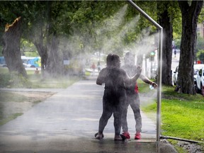 Thaina Duvers and Jams Maxime cool off at a misting station on Mount-Royal Ave. at Esplanade St. on a hot and sticky day in Montreal Monday July 19, 2021.