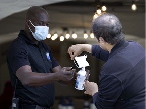 A security guard helps a man disinfect his hands and change face masks before he enters the COVID-19 vaccination centre at the Bill Durnan Arena in Montreal.