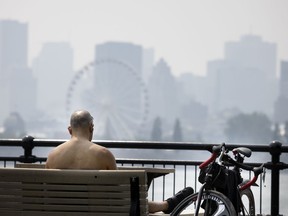 A cyclist enjoys the cool breeze off the water as haze and smog fill the skyline of Montreal as seen from Ile Sainte-Helene, on Monday, July 26, 2021.