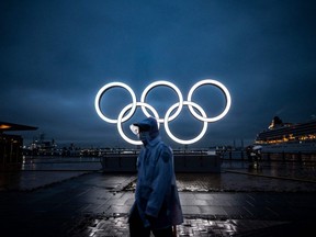 A man walks past the Olympic Rings lit up at dusk in Yokohama on July 2, 2021.