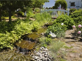 A footbridge spans the cascading stream in the Le Jardin de la Passion Labri rustic country garden.