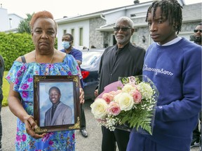 Marie-Mireille Bence holds a photo of her son Jean-René (Junior) Olivier while Olivier's son Kayshawn holds flowers outside Bence's home in Repentigny on Monday August 2, 2021. Olivier was shot by Repentigny police the day before.