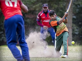 Keeper Hilton Thevan watches as batsman Deavaranjan Ruhishan raises a cloud of dirt as he swings at the ball from bowler Nagendrarasa Prasath during Vezina Cricket League game in Van Horne Park in Montreal on Aug. 7, 2021.