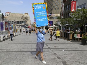 Marie-Hélène from the CIUSSS Centre-Sud de Montréal carries a sign as she tries to recruit people to get vaccinated against COVID-19 at a mobile vaccination clinic in Place des Festivals in Montreal Sunday August 8, 2021.