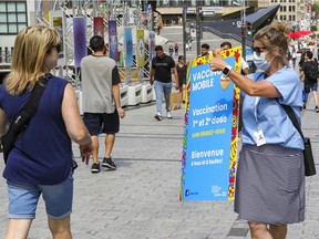 A vaccination worker carries a sign as she tries to recruit people to get vaccinated against COVID-19 at a mobile clinic in Place des Festivals in Montreal Sunday August 8, 2021.