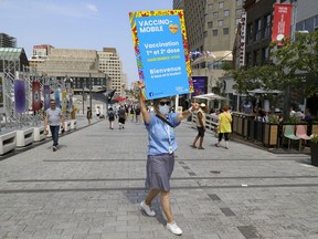Marie-Hélène from the CIUSSS Centre-Sud de Montréal carries a sign as she tries to recruit people to get vaccinated against COVID-19 at a mobile vaccination clinic in Place des Festivals in Montreal on August 8, 2021.