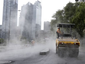 Steam rises off the hot asphalt as rain falls on a crew paving Peel Street in the Griffintown district of Montreal on August 9, 2021.