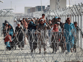 Afghans walk along fences as they arrive in Pakistan through the Pakistan-Afghanistan border crossing point in Chaman on Aug. 24, 2021.