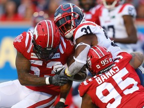 Montreal Alouettes William Stanback is tackled by Darnell Sankey and Stefen Banks of the Calgary Stampeders during CFL football in Calgary on Friday, August 20, 2021.