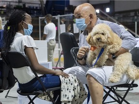 Zootherapist Sylvain Gonthier and dog Bidule comfort Divine Nsabimana as she waits to receive a COVID-19 vaccine at a clinic in Montreal, Thursday, Aug. 26, 2021.